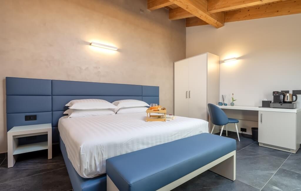 Camera d'hotel moderna con letto, scrivania e illuminazione calda. Pavimento in piastrelle grigie scure.