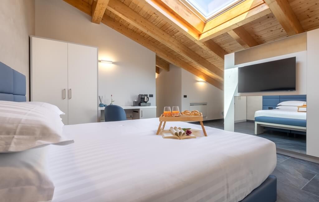 Camera d'hotel moderna con letti, mobili blu, luce naturale e un vassoio con succhi e dolci sul letto.