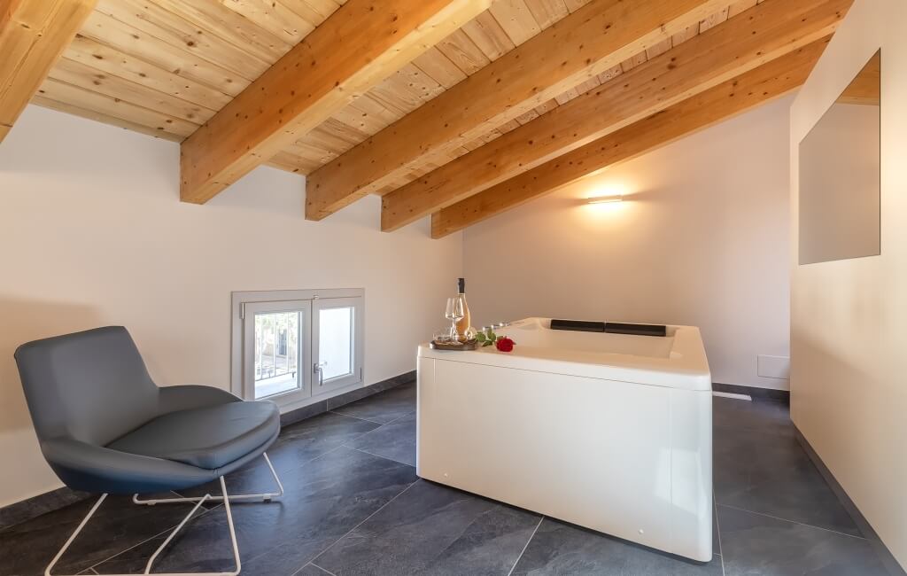 Bagno moderno e sereno con vasca bianca, travi in legno a vista, pareti bianche e pavimento in piastrelle grigie scure.