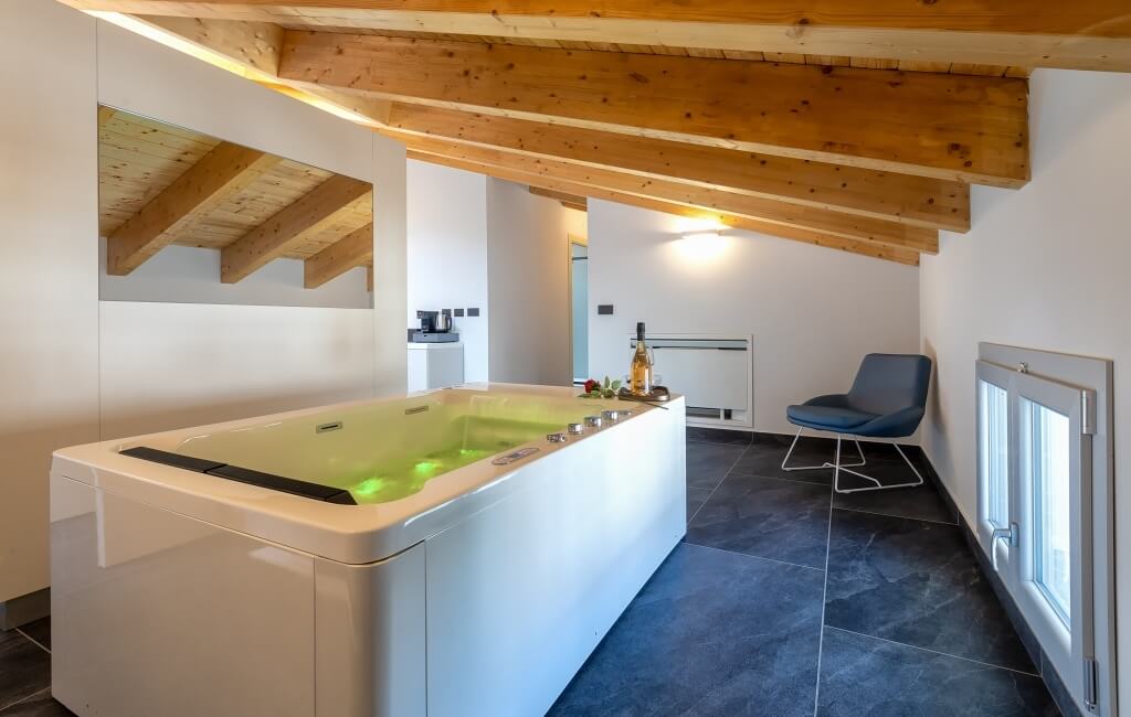 Bagno moderno con vasca bianca, sedia grigia e finestra, illuminato da luci verdi e decorato con champagne e fiori.