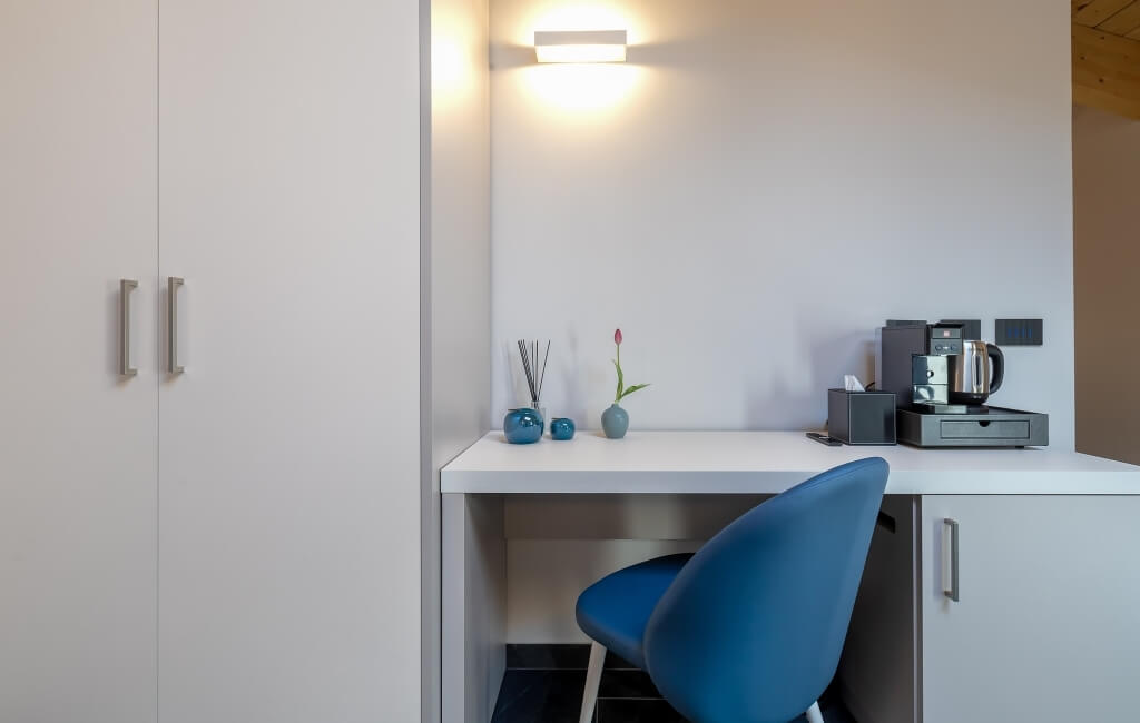 Spazio di lavoro moderno con scrivania bianca, sedia blu, decorazioni eleganti e angolo caffè a destra.