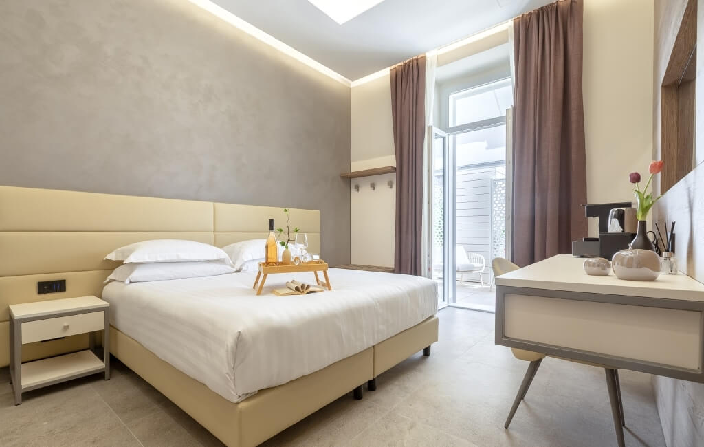 Camera d'hotel elegante con letto bianco, comodino moderno e scrivania, decorata in toni neutri e accoglienti.