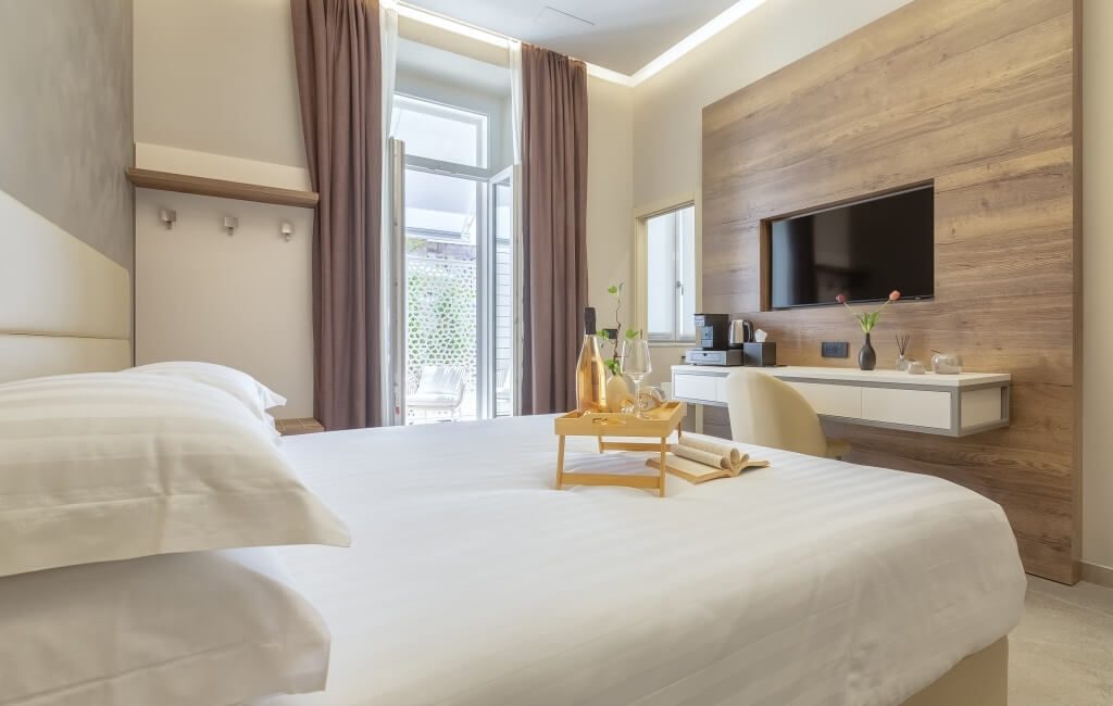 Camera d'hotel serena con letto grande, champagne, libro aperto e accesso a un balcone. Atmosfera rilassante e accogliente.