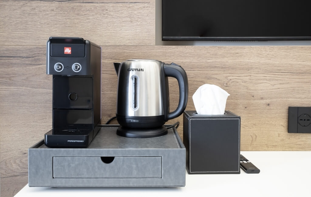 Contatore di hotel con macchina da caffè Nespresso, kettle De'Longhi, scatola di fazzoletti e telecomando su sfondo moderno.