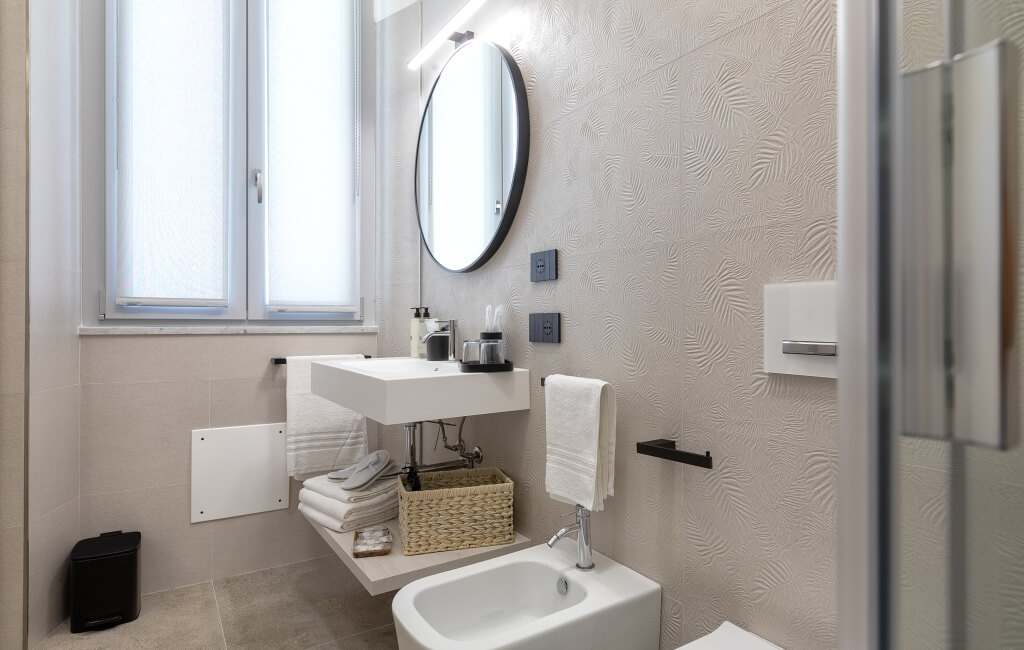 Bagno moderno e minimalista con lavabo, specchio, scaffale bianco e asciugamani, pareti con carta da parati a foglie.
