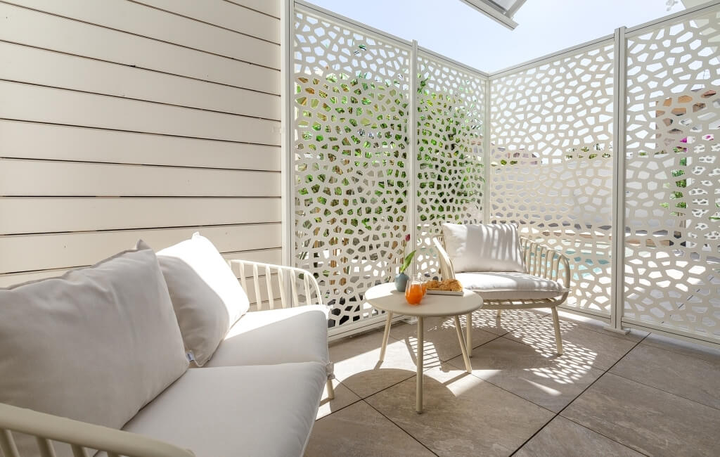 Area esterna serena con divano bianco, sedia e tavolo rotondo, decorata con un drink e una pianta in un vaso.