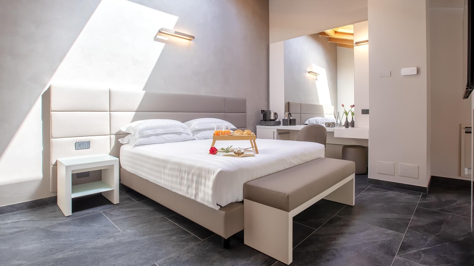 Camera d'hotel moderna con letto grande, scrivania, specchio, e decorazioni come un vassoio con succo d'arancia e dolci.