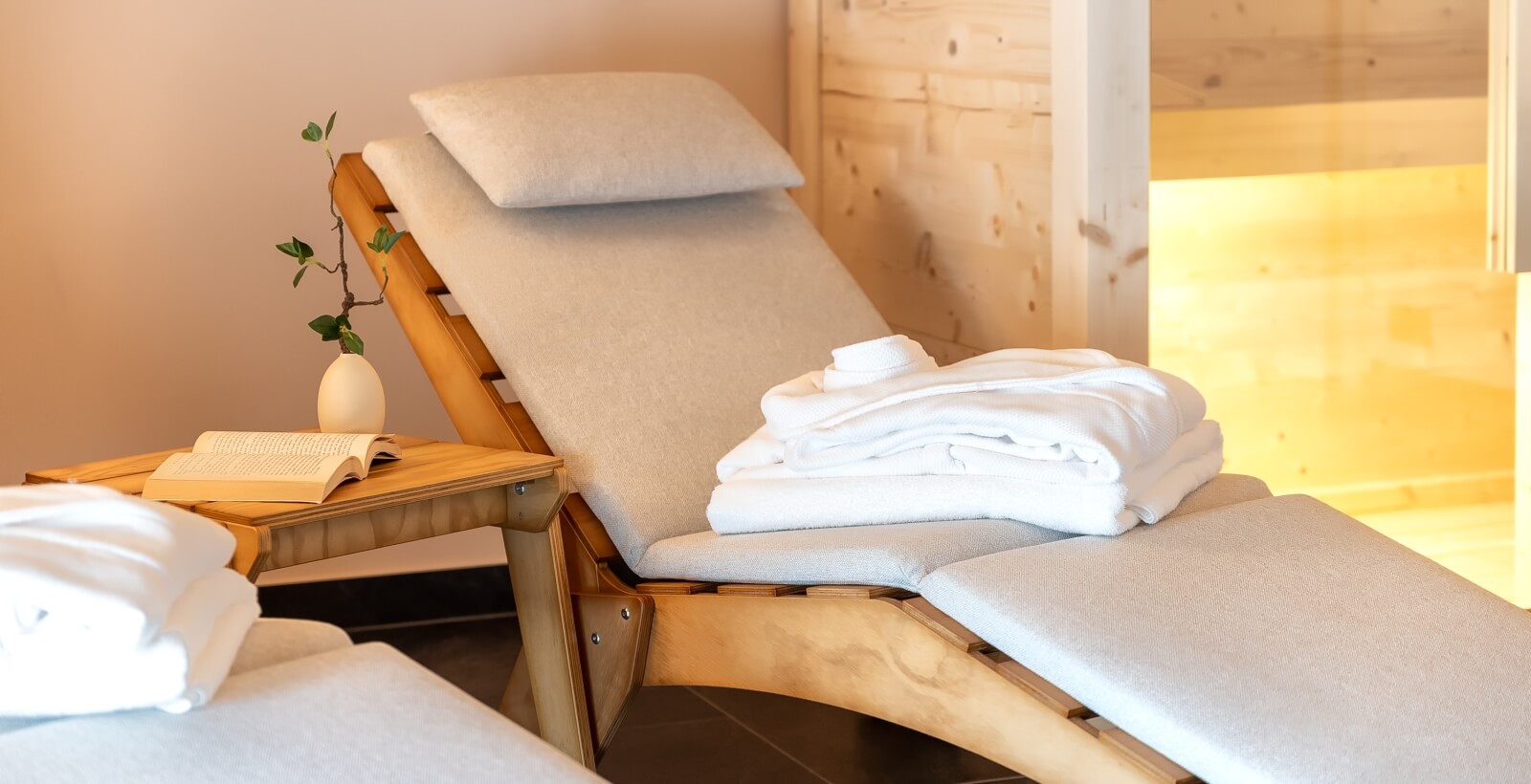 Chaise lounge con accappatoi bianchi, tavolino con vaso e libro, pareti in tonalità calde, atmosfera di relax.