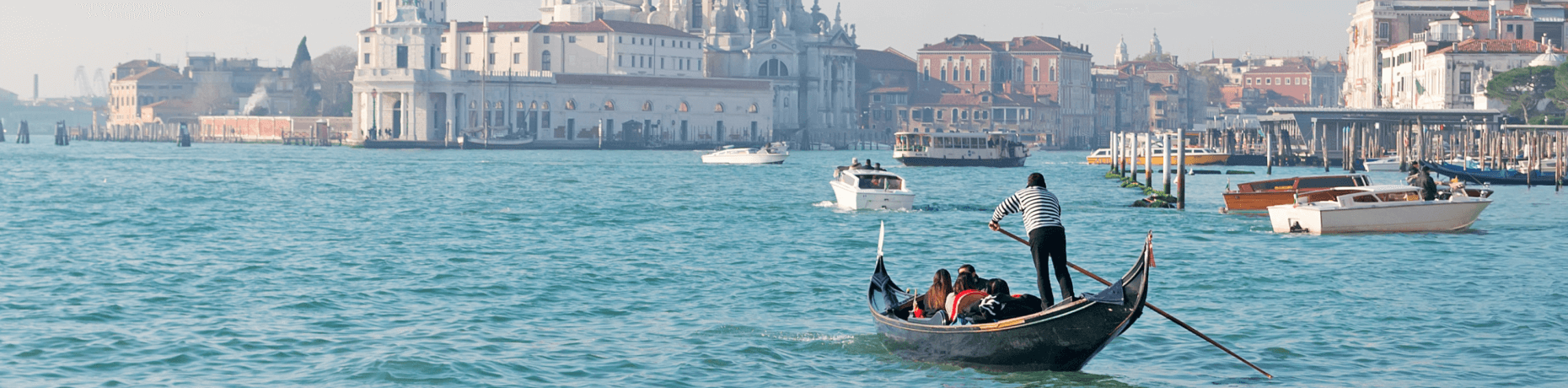 Gondoliere in una gondola nera naviga acque calme con passeggeri, mentre edifici storici si stagliano sullo sfondo.