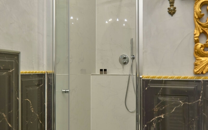 Doccia con soffione argentato, porte in vetro e piastrelle marmorizzate.