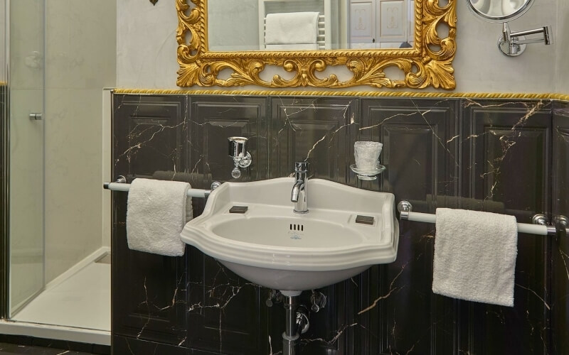 Bagno d'hotel con lavabo bianco, specchio dorato e doccia.