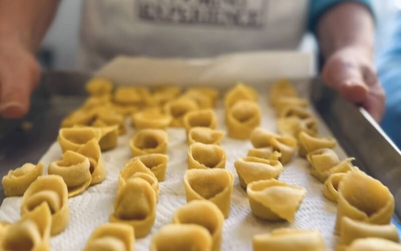 Vassoio con pasta cruda su carta assorbente, persona in sfondo.