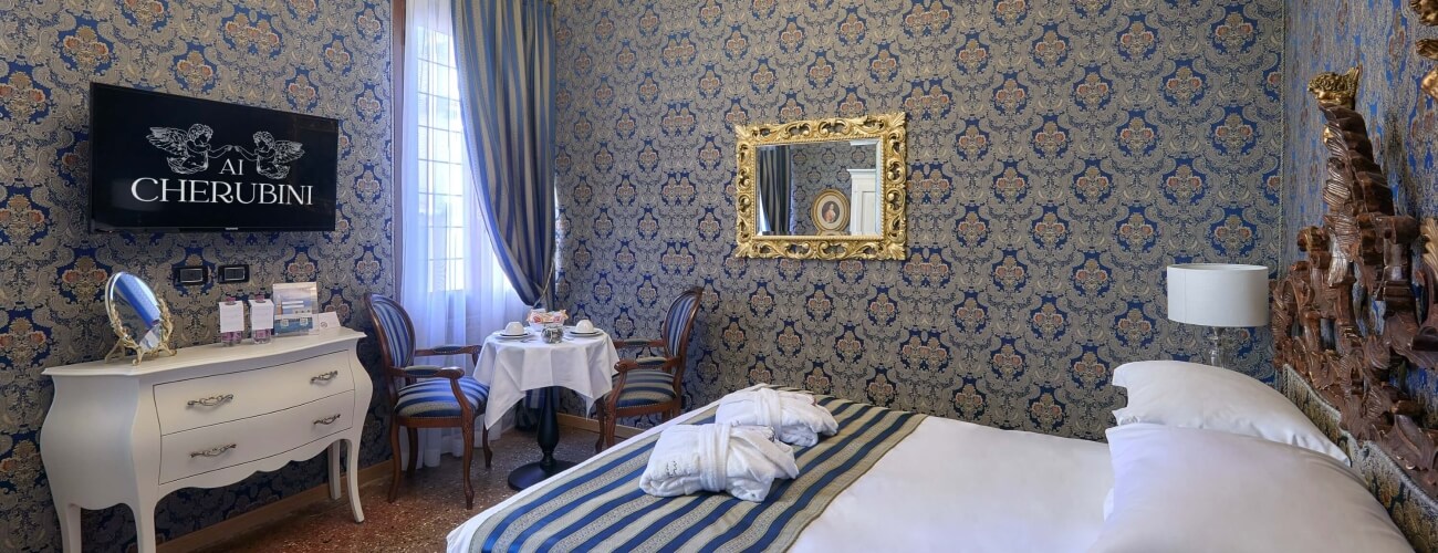 Luxurious hotel room featuring a bed, dresser, table, and elegant decor with blue and gold wallpaper.