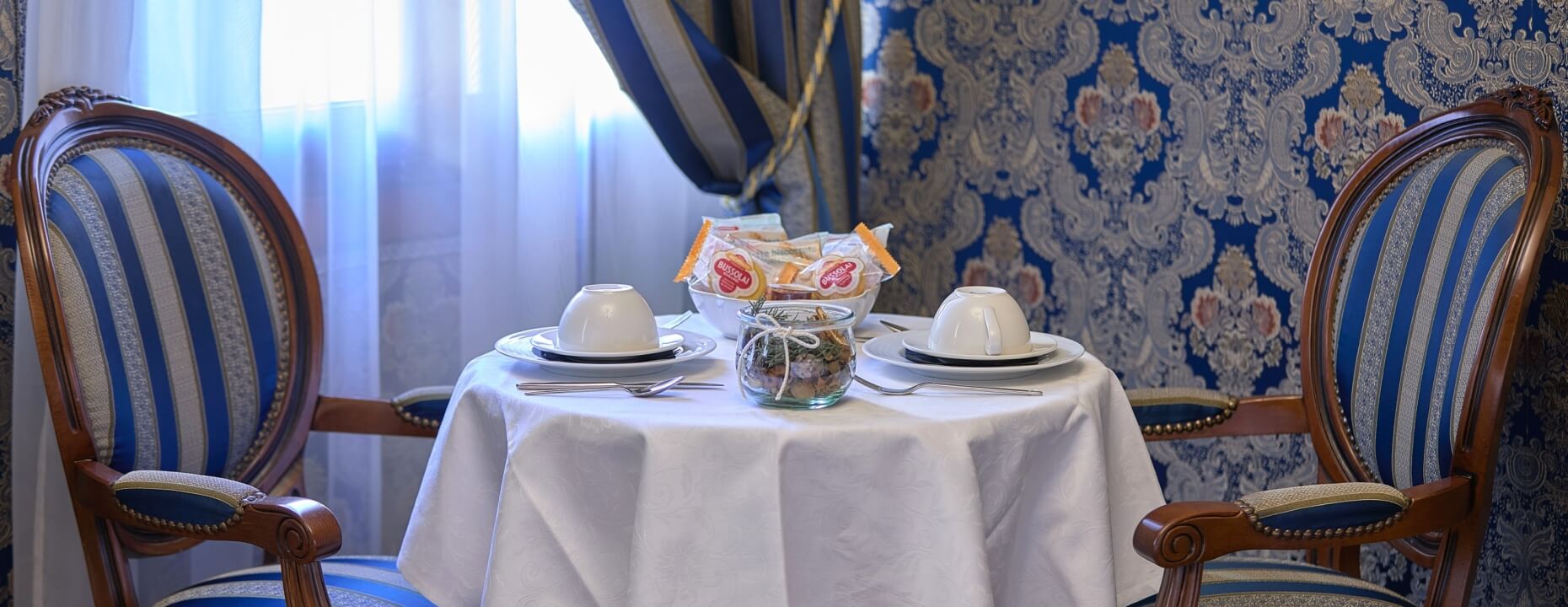 Due sedie ornate con tessuto a righe, tavolo decorato con stoviglie.