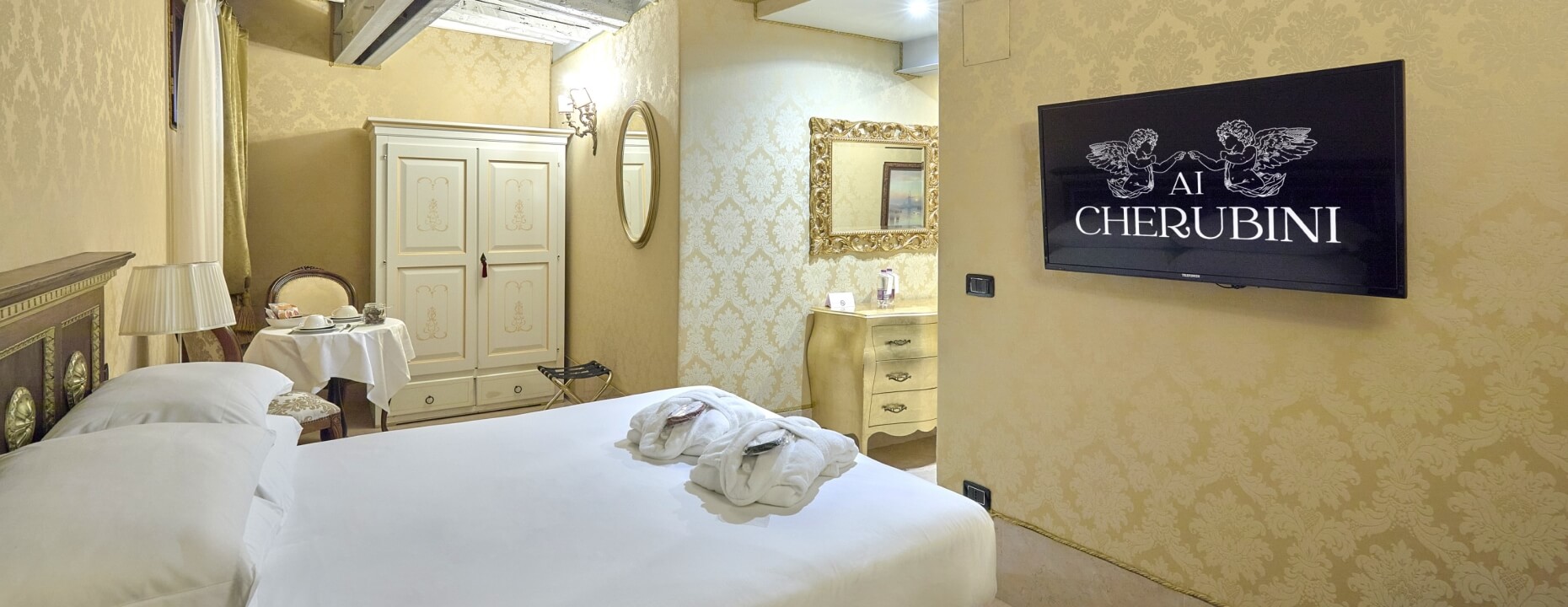 Camera d'hotel con letto, tavolo, armadio e TV montata.