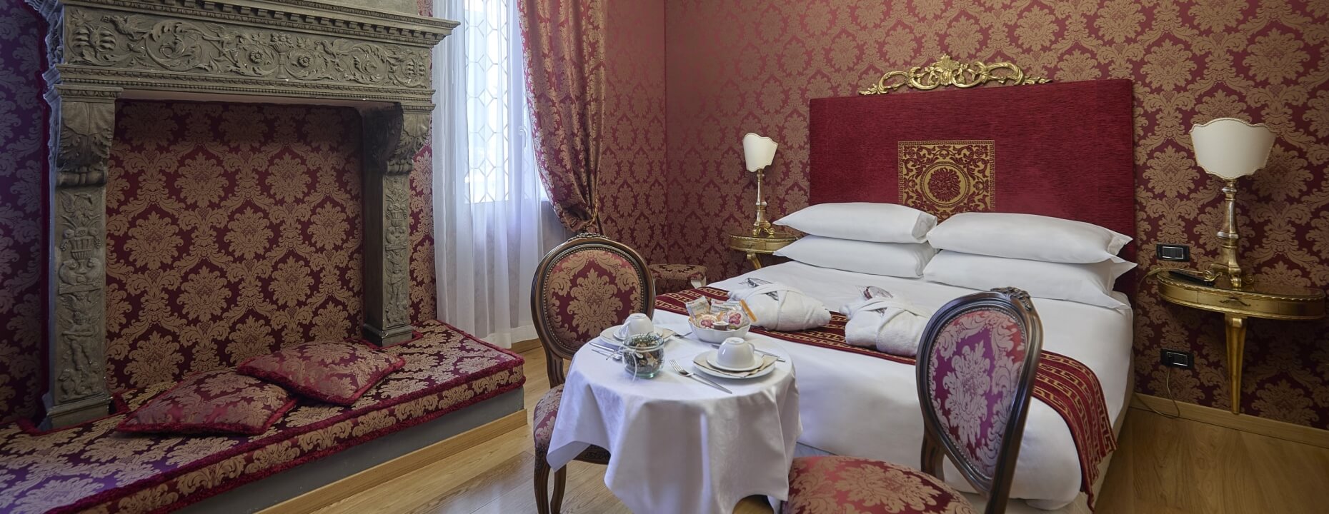 Camera d'hotel con letto grande, camino e pareti damascate rosse.