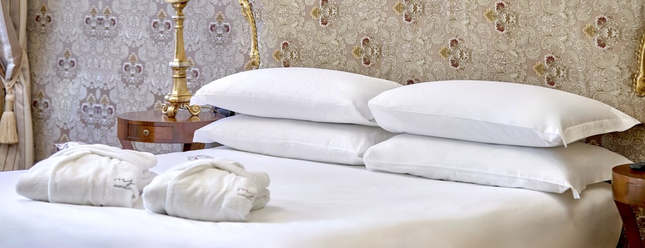 Camera d'hotel con letto bianco, accappatoi e carta da parati damascata.
