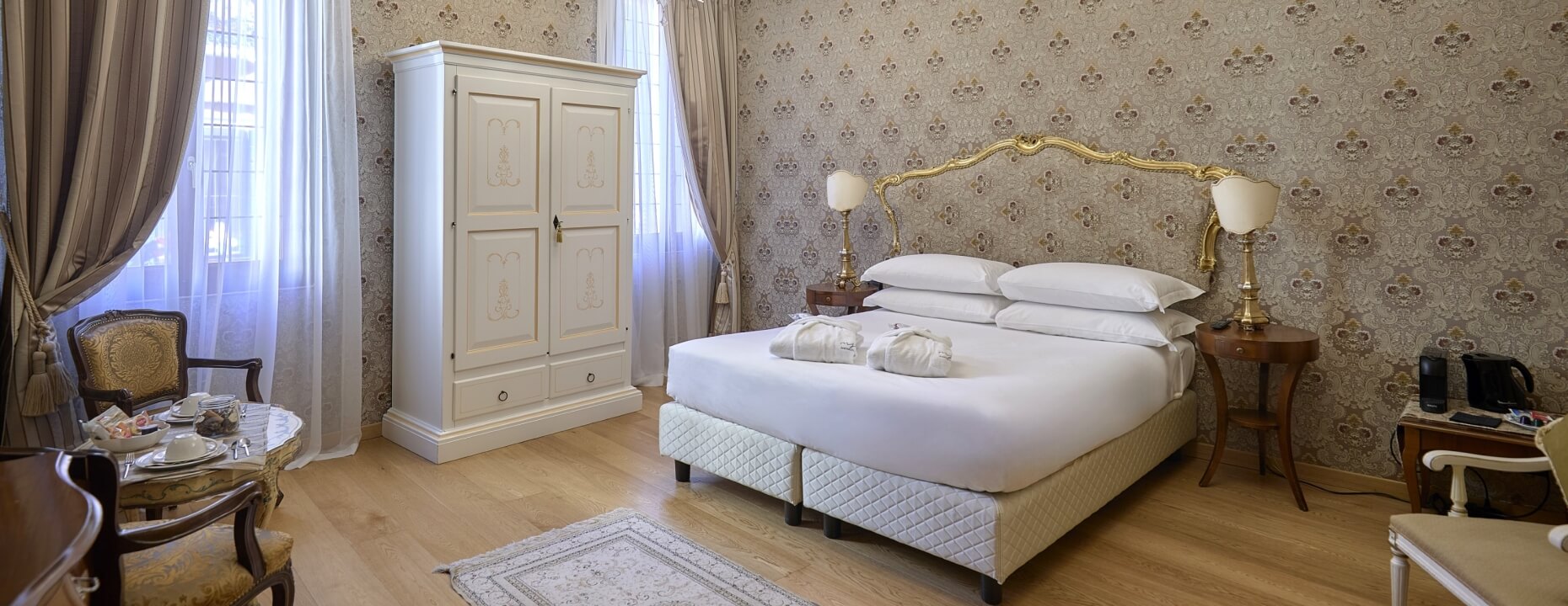 Camera d'hotel con letto grande, armadio, tavolo e finestre.