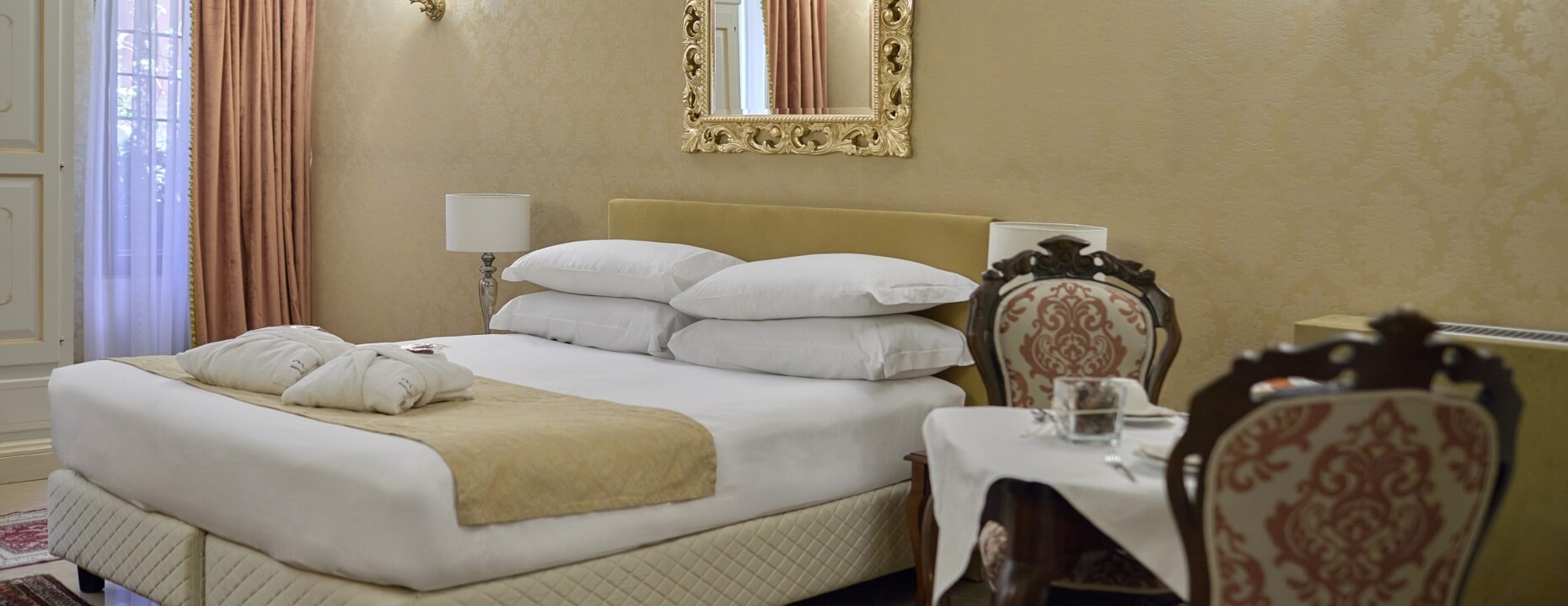 Camera d'hotel con letto king-size, tavolo e specchio dorato.