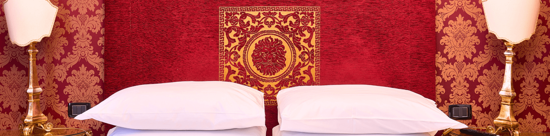 Luxuriöses Schlafzimmer mit zwei identischen Betten, rotem und goldfarbenem Wandmuster, Nachttischen und eleganten Lampen.