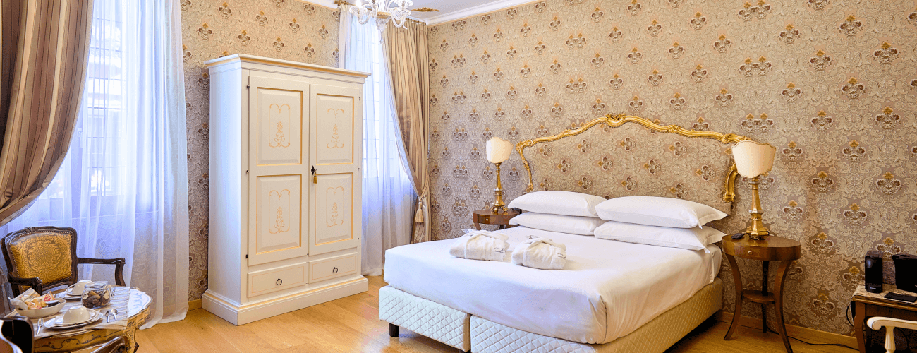 Serene bedroom with a white bed, floral wallpaper, natural light, and cozy furniture, exuding tranquility and relaxation.