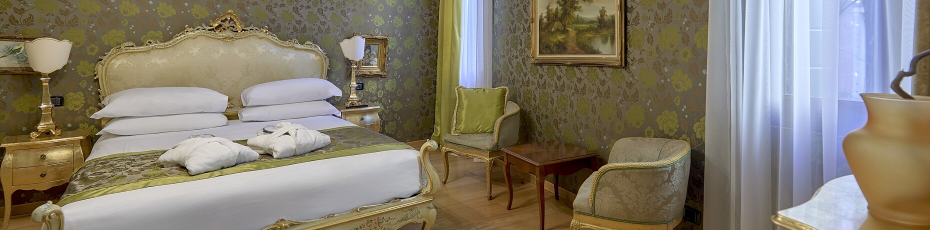 Camera d'hotel elegante con letto, tavolino, sedie e vasi decorativi, pareti con carta da parati floreale.
