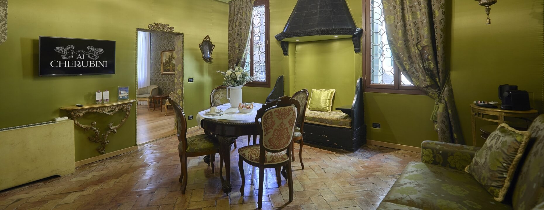 Camera d'hotel con pareti verdi, tavolo da pranzo e divano.