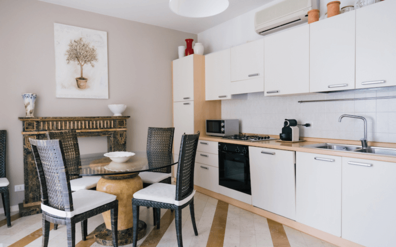 Moderne Küche mit weißen Schränken, Essbereich, Glas-Esstisch, Kamin und dekorativem Baumgemälde.