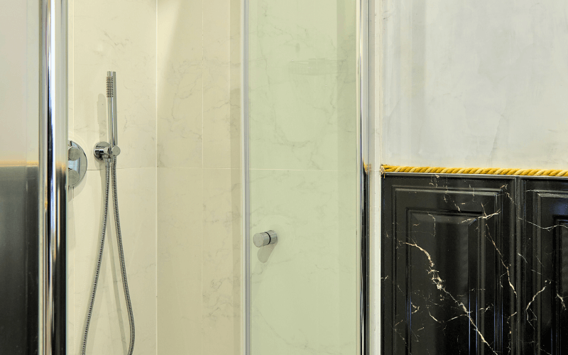 Luxuriöses Badezimmer mit Duschkabine, cremefarbenen Wänden, schwarzem und gelbem Marmor sowie eleganten Designelementen.