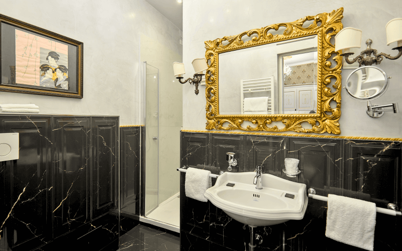 Luxurious black and white bathroom with gold accents, featuring a sink, mirror, towel racks, shower enclosure, and artwork.