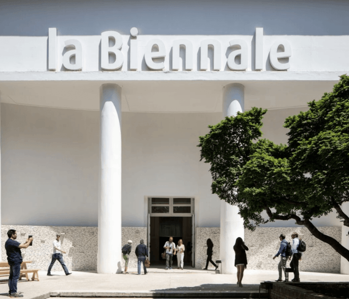 Edificio con "la Biennale", persone all'ingresso e albero verde.
