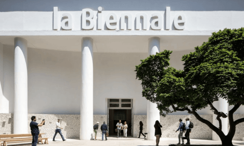 Esterno di un edificio bianco con "la Biennale" e persone.