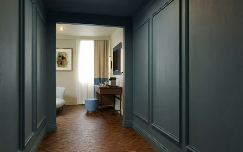 Corridoio blu scuro conduce a una stanza con divano bianco e ottomano blu.