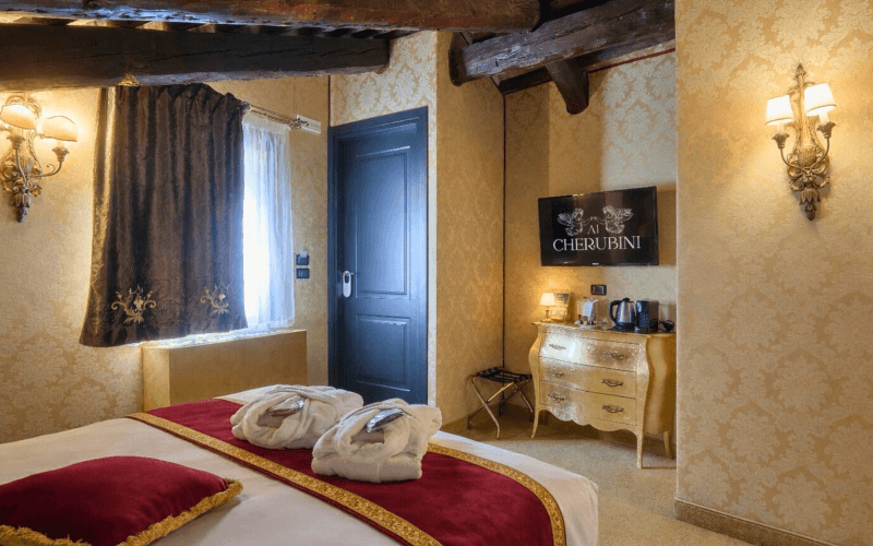 Camera d'hotel con letto, TV, armadio e soffitto a travi.