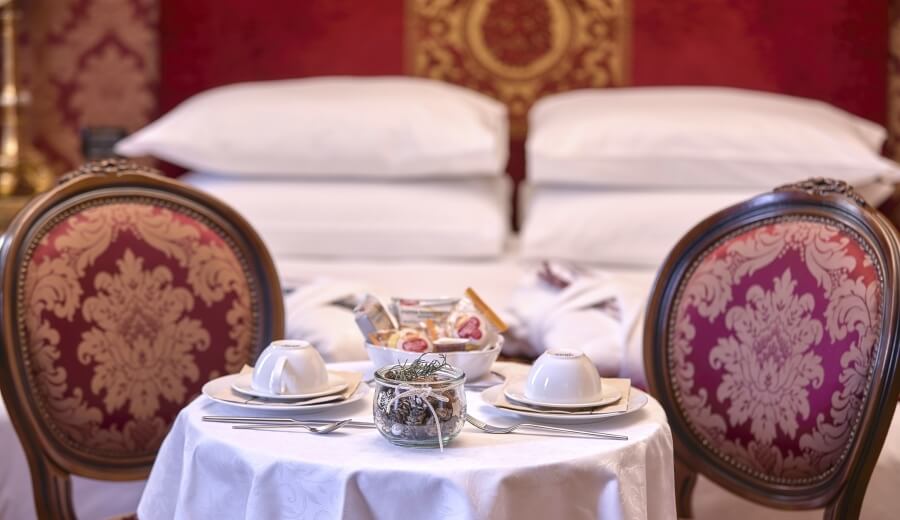 Tavolo rotondo per due con piatti, tazze e dolci, letto elegante sullo sfondo in una camera di lusso.