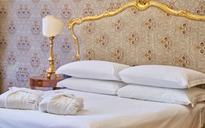 Camera d'hotel con letto bianco, cuscini e accappatoi piegati.
