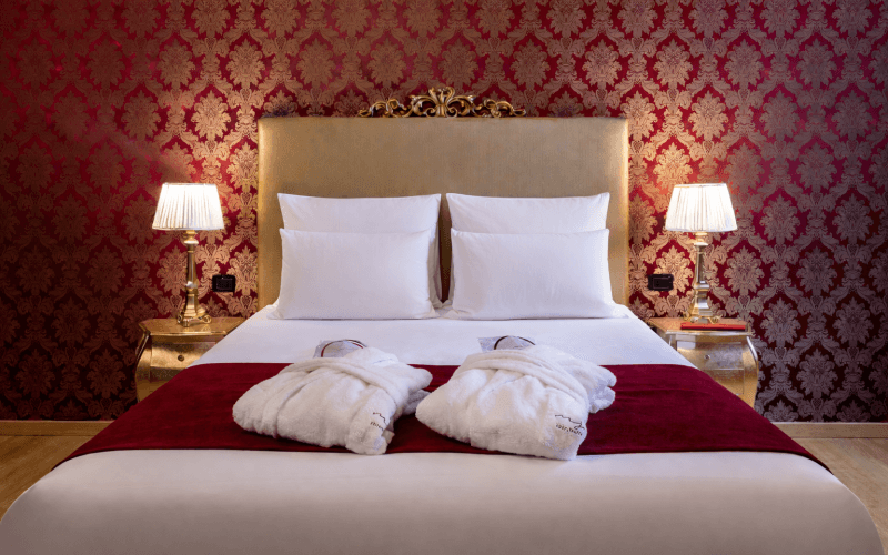 Camera d'hotel con letto bianco, runner rosso e pareti damascate.