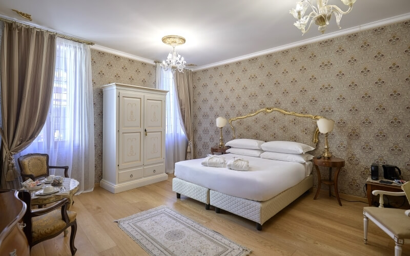 Chambre luxueuse avec un grand lit, une commode, une table pour deux et des détails élégants.