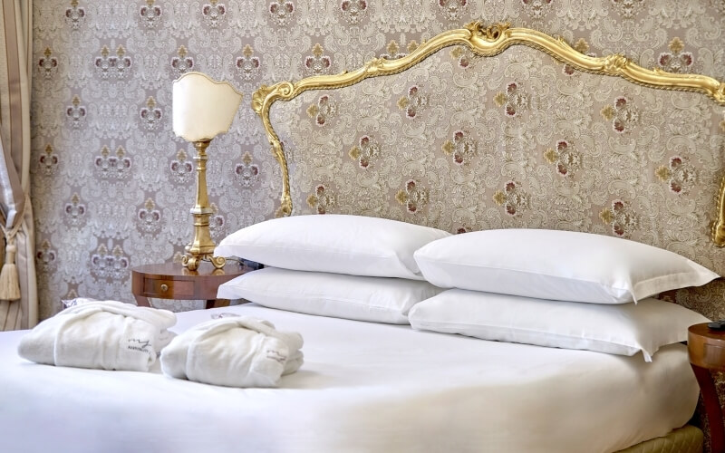 Chambre d'hôtel avec lit, peignoirs, lampes dorées et motifs damassés.