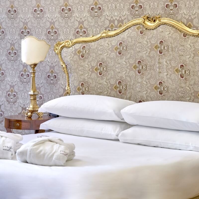 Camera d'hotel con letto bianco, cuscini e accappatoi piegati.