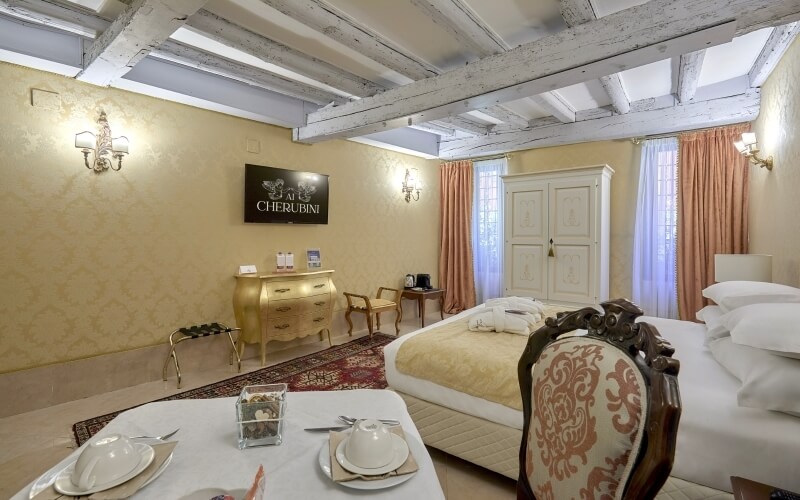 Chambre d'hôtel luxueuse avec plafond haut, table pour deux, lit king-size, fenêtres du sol au plafond et ambiance chaleureuse.