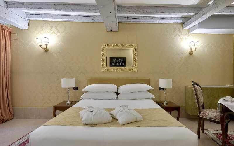Chambre d'hôtel avec lit king-size, deux tables de nuit, coin repas, décorée en or et blanc.