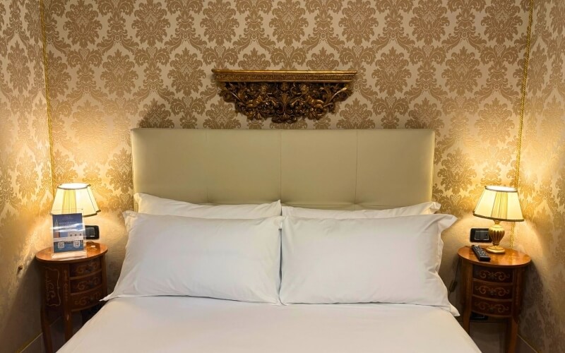 Camera d'hotel con letto, testiera beige e parete dorata.