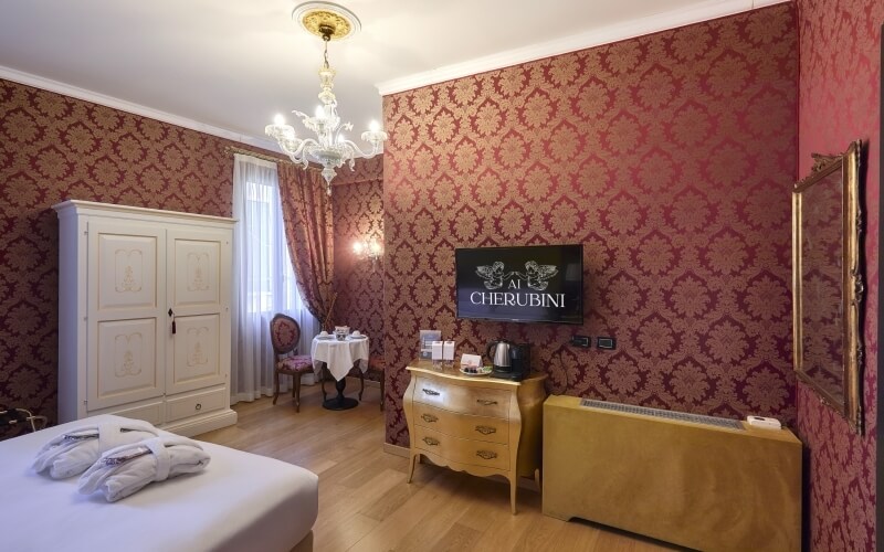 Chambre luxueuse avec lit blanc, TV, bureau, armoire, lustre, miroir, fenêtre avec rideaux, et sol en bois.