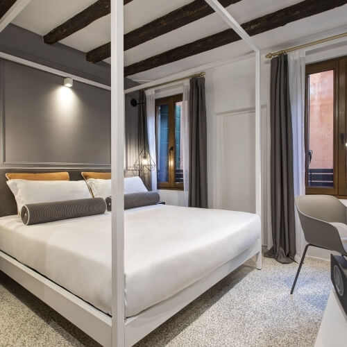 Camera d'hotel con letto a baldacchino e decorazioni grigie e bianche.