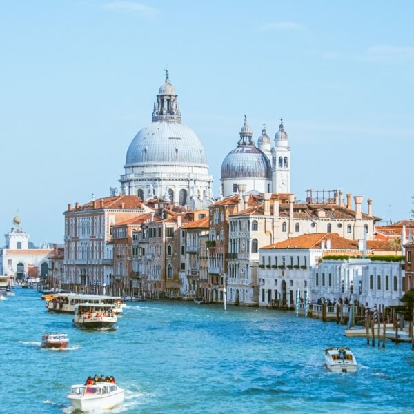 Canale Grande a Venezia con chiesa bianca, barche e cielo blu, evocando serenità e bellezza.