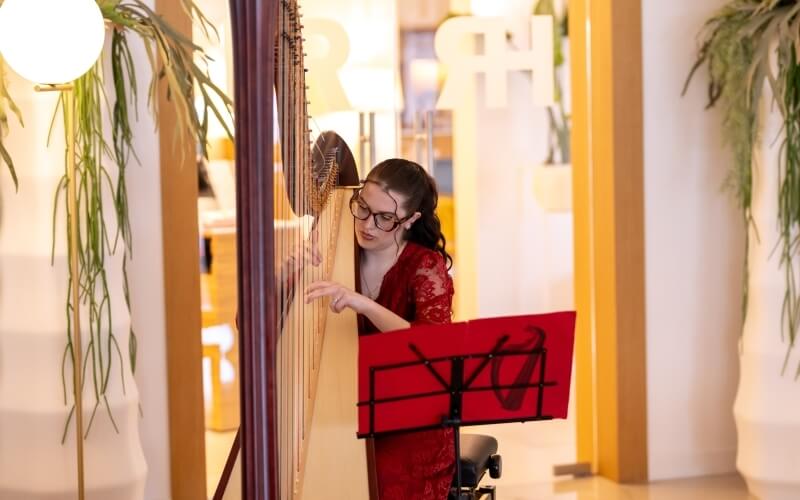 Donna con occhiali in abito rosso suona l'arpa.