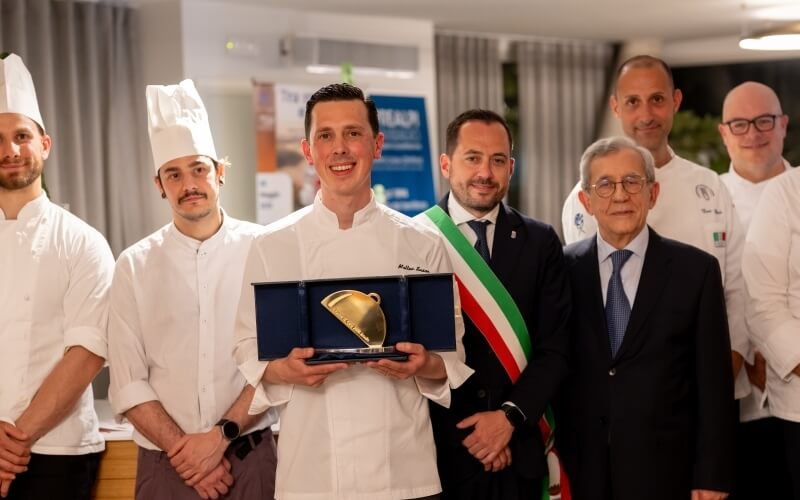 Uomini in divisa da chef con trofeo, sorridendo per foto.