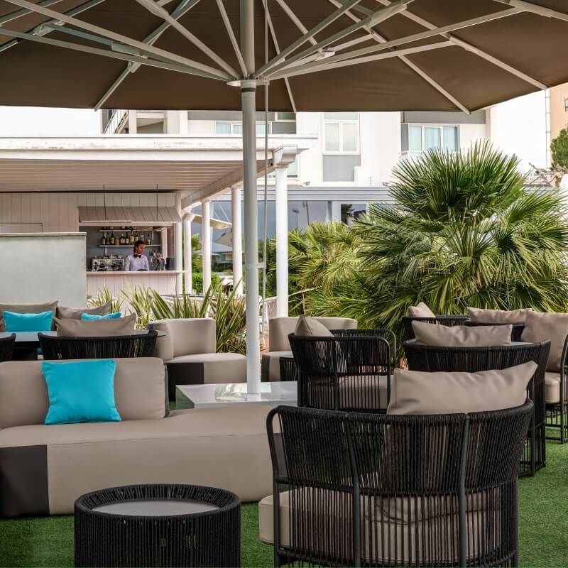 Outdoor seating area with beige sofas, dark wicker, and palm trees.