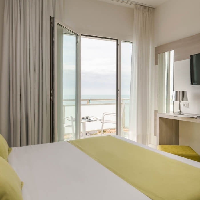 Camera d'hotel elegante con vista sull'oceano, letto bianco, decorazioni neutre e atmosfera rilassante.